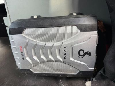 Kenworth T680 engine bay with a portable Cobbler COber 2500W inverter/auxiliary power unit mounted in the cab area showing a rugged silver casing with black top and textured fins.