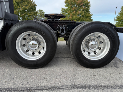 Dual rear wheels of a 2021 Kenworth T680 tractor showing polished steel rims and tires, with undercarriage components and leaf spring area visible.