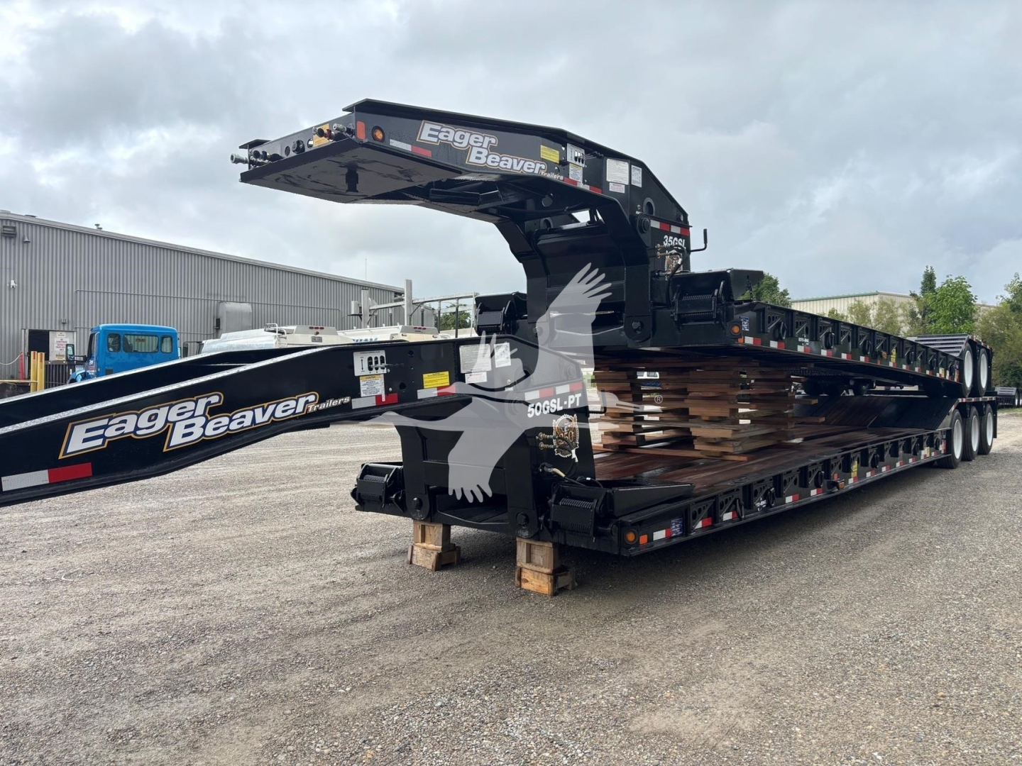 Trailer showing a black Eager Beaver 35Gsl-S lowboy with gooseneck crane, stacked steel deck sections, and white Eager Beaver logo on the side.