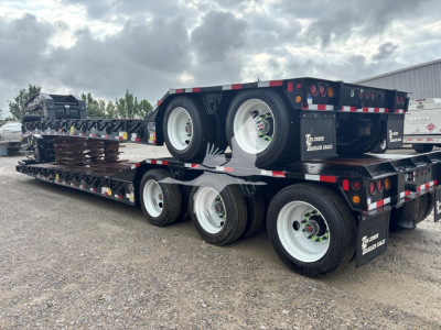 Trailer stacked with flatbed loads showing dual rear axles and white rims; black flatbed trailers with reflective red/white safety stripes and dual tires.