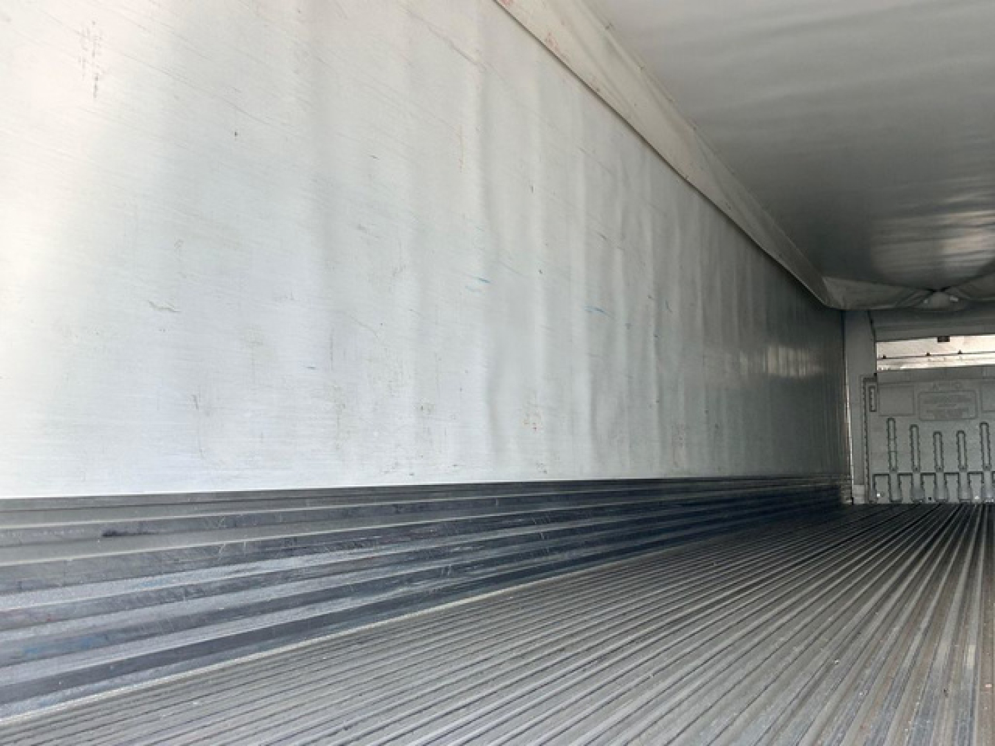 Trailer interior showing ribbed metal floor and sidewall with light reflections inside a refrigerated trailer.