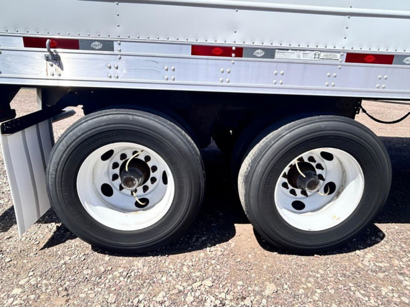 Trailer axle area showing dual rear wheels and lower side of refrigerated trailer with riveted metal siding.