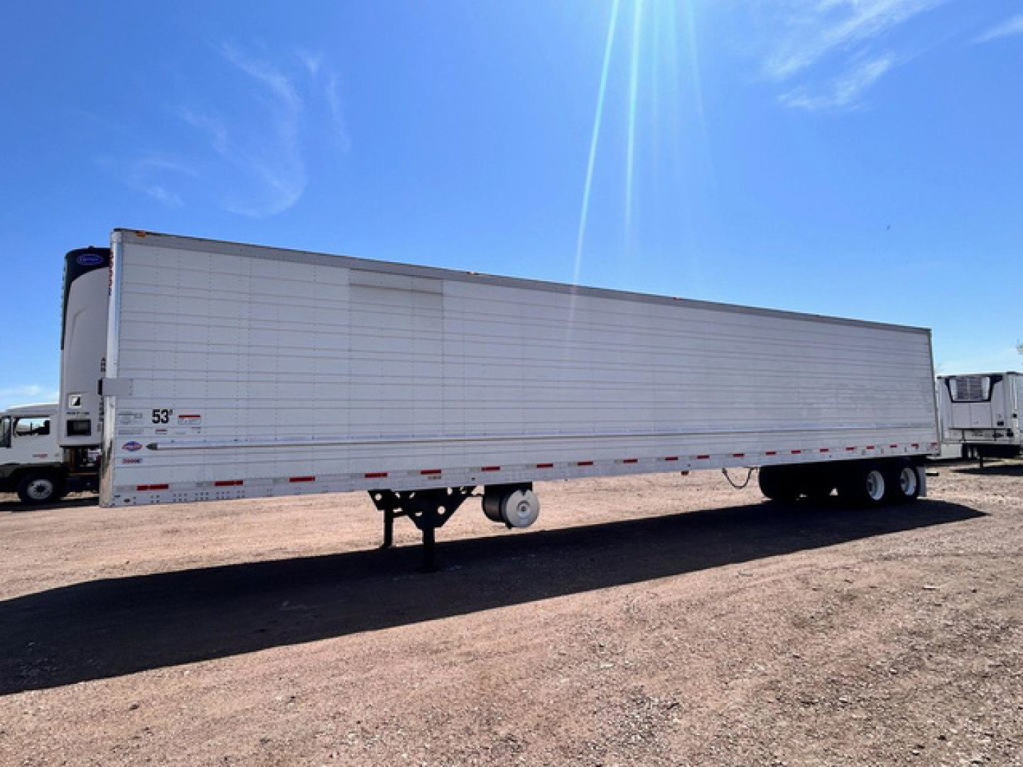 Trailer side view of a 2022 Utility Reefer with white exterior and dual rear axles, parked on dirt lot.