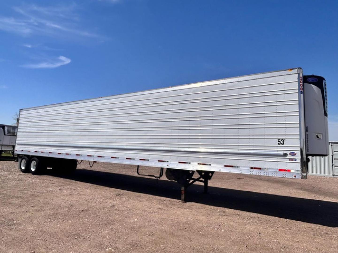 Trailer side view of a 53 ft refrigerated utility trailer with metal ribbed exterior and tandem axles under clear sky.