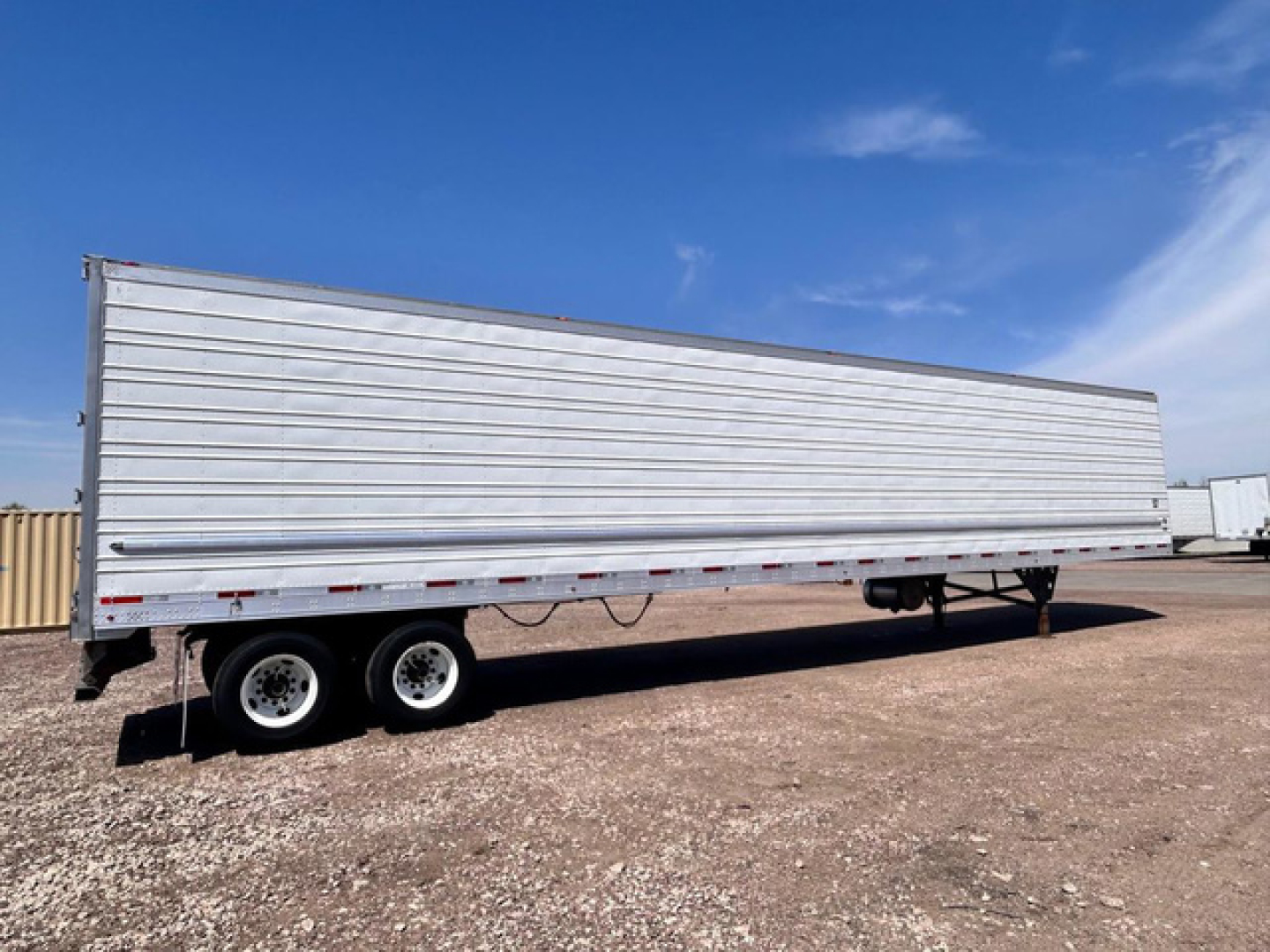 Utility reefer trailer with aluminum side panels and tandem axles, side view showing long rectangular cargo area and landing gear.