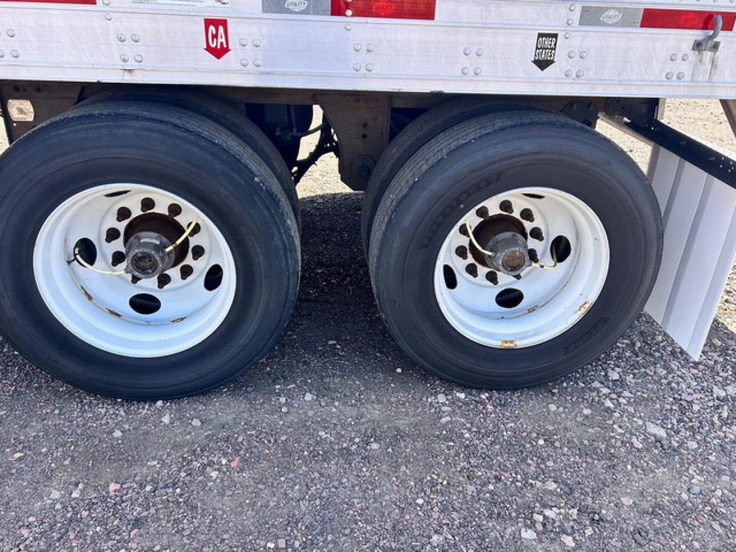 Twin rear wheels of a refrigerated trailer with white rims and black tires; side of trailer shows stickers and small text near top edge.