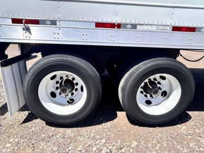 Trailer axle area showing dual rear wheels and lower side of refrigerated trailer with riveted metal siding.