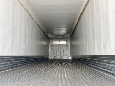 Interior of a refrigerated trailer showing the empty ribbed metal floor and white walls, with a rear door and trailer ceiling visible.