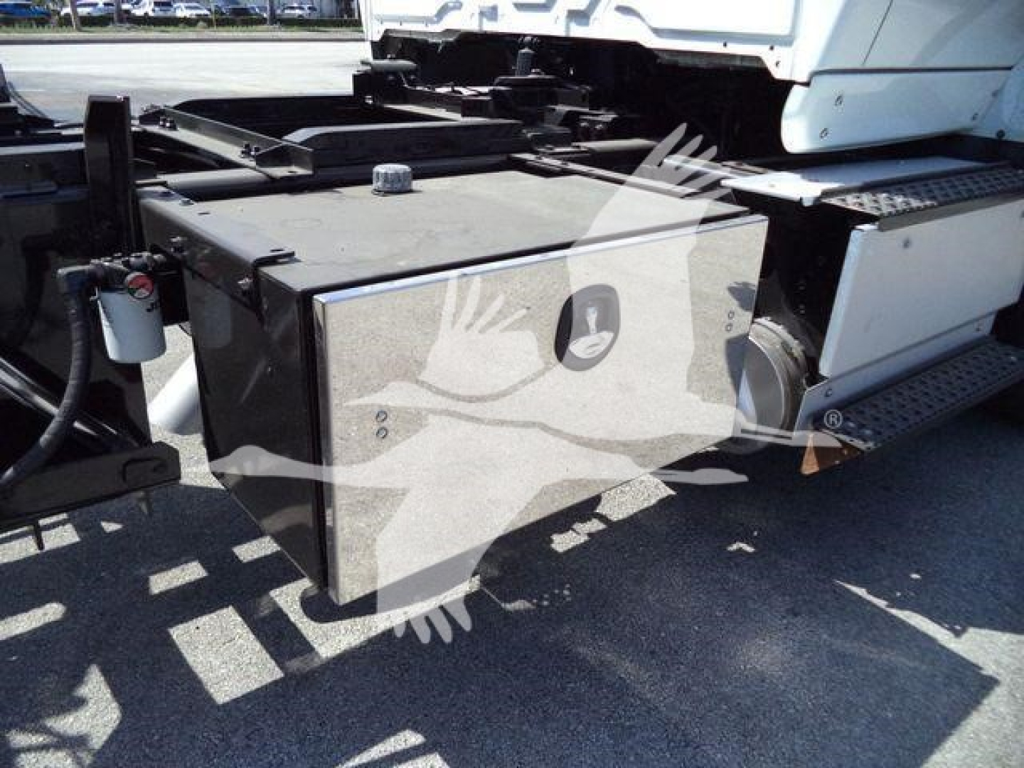 Trailer truck chassis with a rectangular fuel or storage tank mounted beside the cab; visible box with a round cap, side steps, and hydraulic lines; general vehicle components in view.