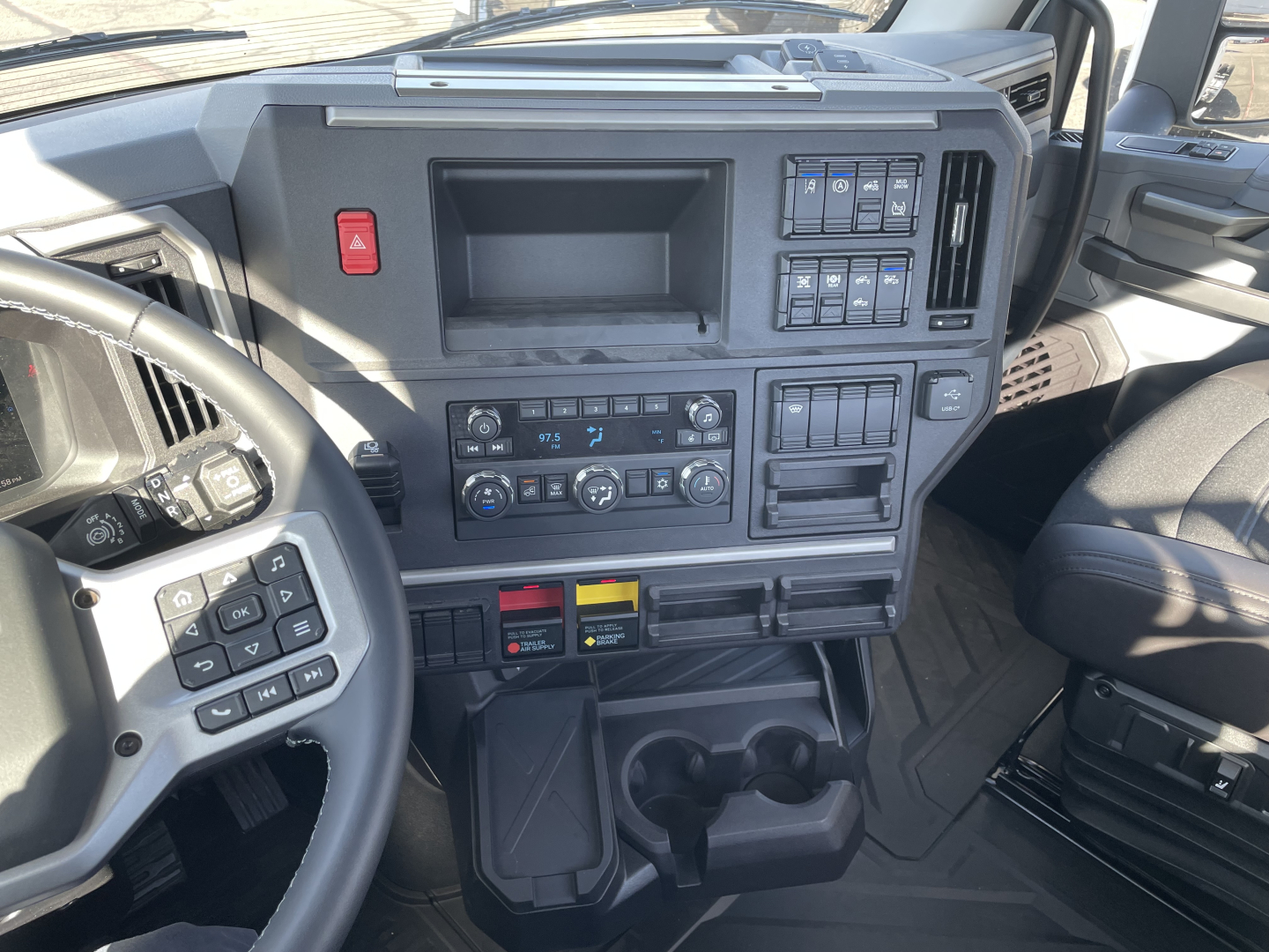 Mack PR64T truck interior showing dashboard and steering wheel with control panels, cupholders, and center console.