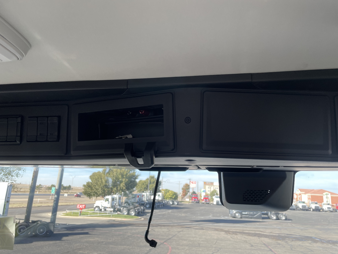 Dashboard area of a 2026 Mack PR64T cab showing overhead compartments and a hanging cord with a screen compartment.