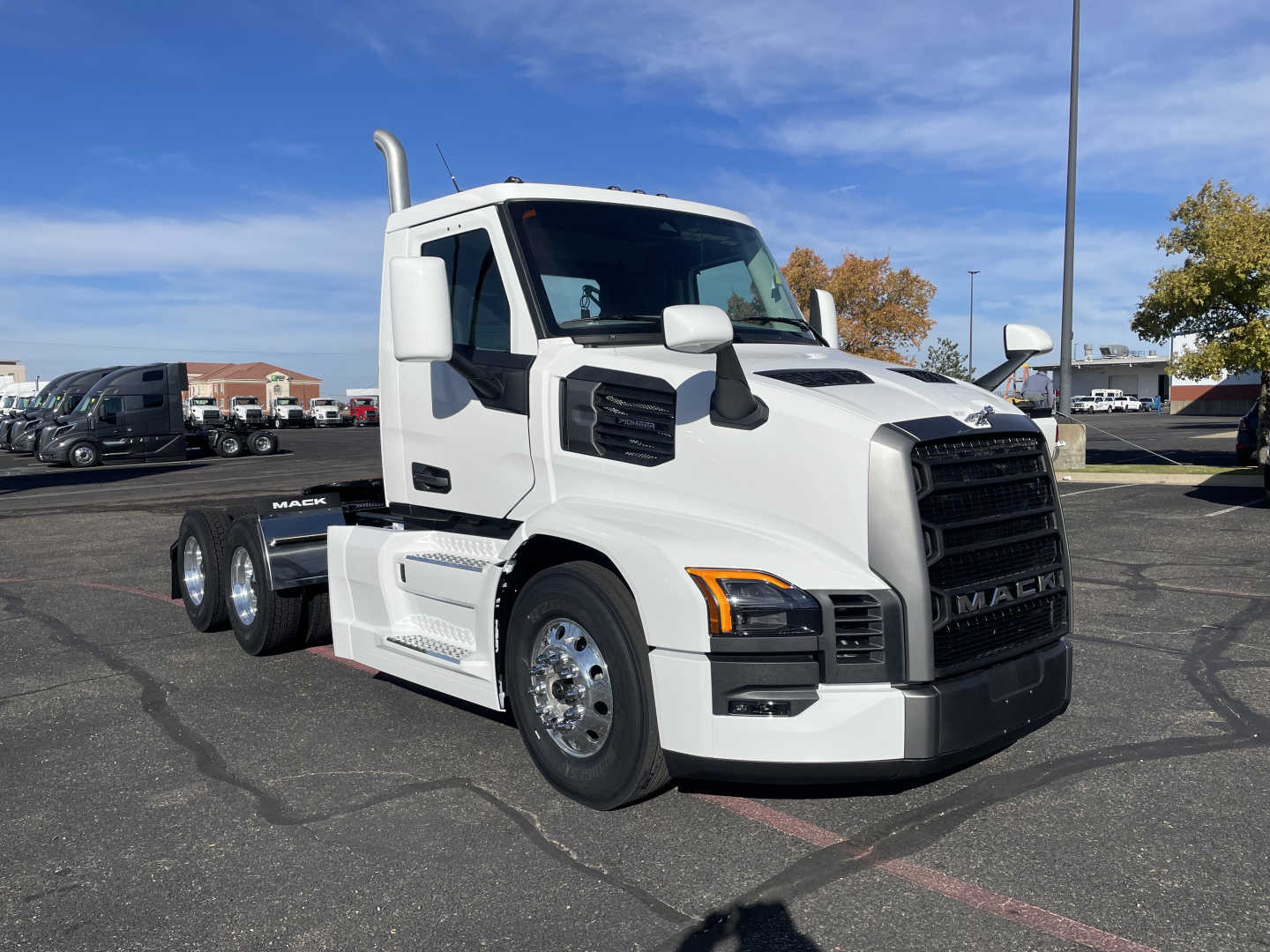 White Mack PR64T conventional daycab semi-truck in a dealership lot, front three-quarter view with large grille, black bumper, and dual rear axles.