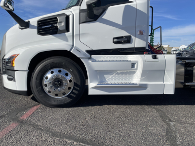 Front-side view of a white 2026 Mack PR64T conventional daycab truck showing front wheel, cab step, and fuel/air hoses; text not legible on components visible.
