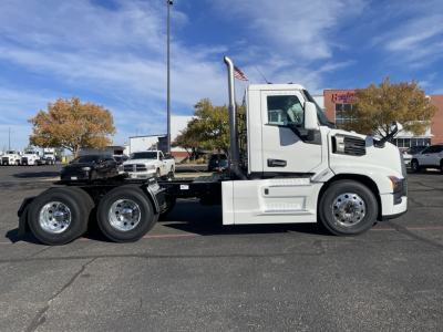 Truck chassis side profile of a white Mack PR64T tractor in a parking lot, showing cab, low air intake, and dual rear axles with chrome wheels.