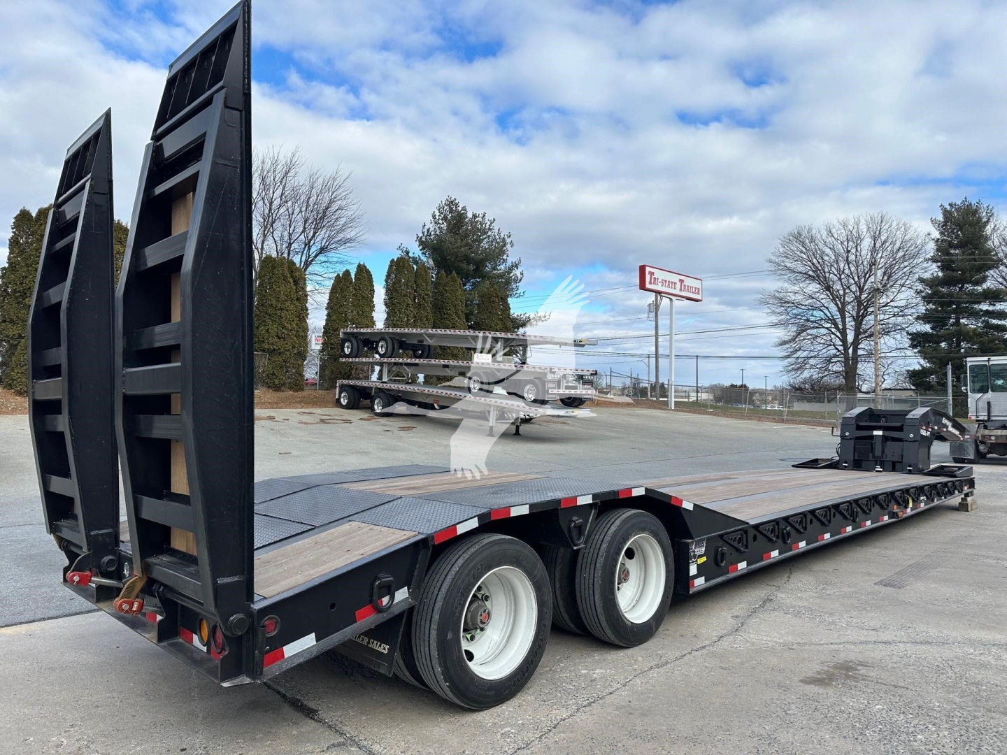 Trailer deck with ramp legs raised showing lowboy flatbed and dual rear tires; black steel ramps at rear, stock number TL088496 visible.