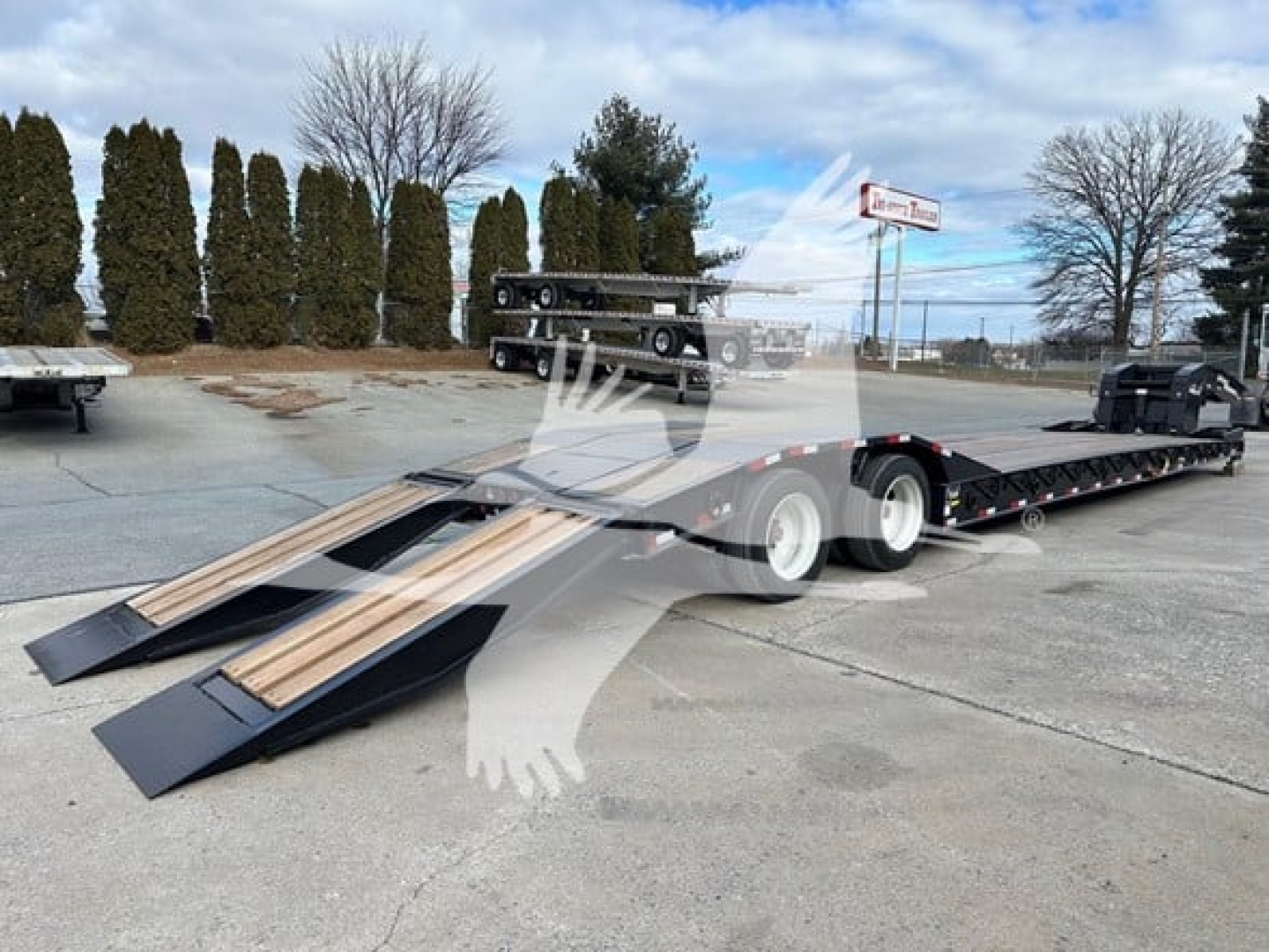 Trailer photo showing a lowboy trailer with loading ramps and wooden deck sections, front cab and wheelset visible, outdoor lot.