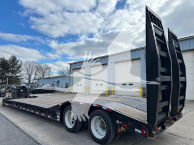 Lowboy trailer with long flat deck and ramps upright at rear, black metal frame, dual rear axles