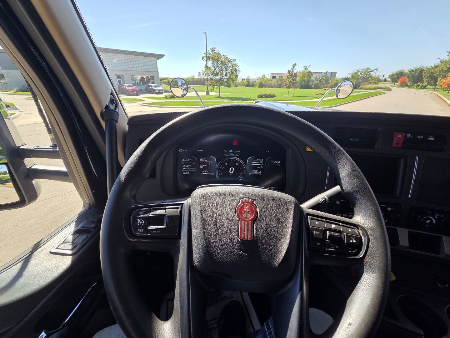 Kenworth W990 cabin steering wheel and dashboard view from driver seat, front windshield with side mirrors, infotainment and controls visible.