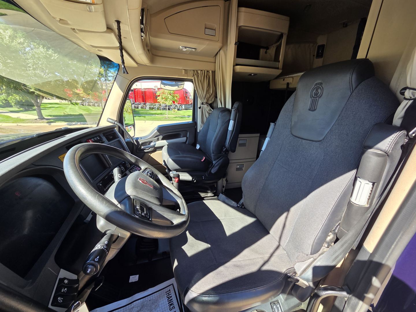 Kenworth W990 truck interior showing driver seat, steering wheel, and front cabin area with side window and overhead storage.