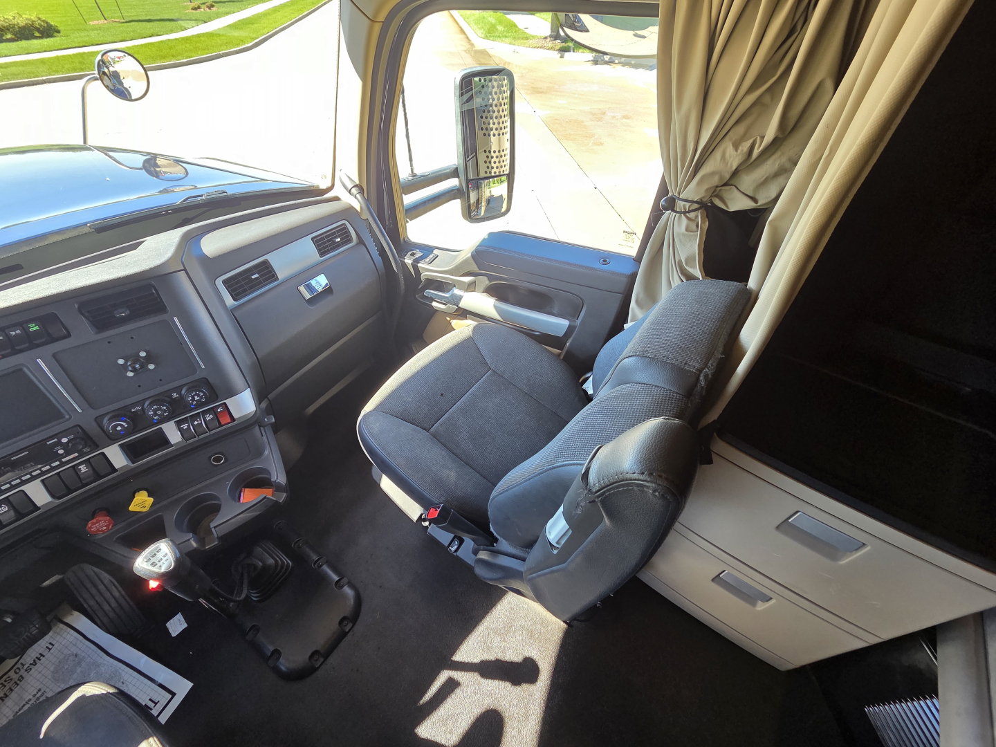 Kennworth W990 truck interior front cabin view with driver seat, steering wheel, dashboard, and side window; curtain visible by sleeper area.