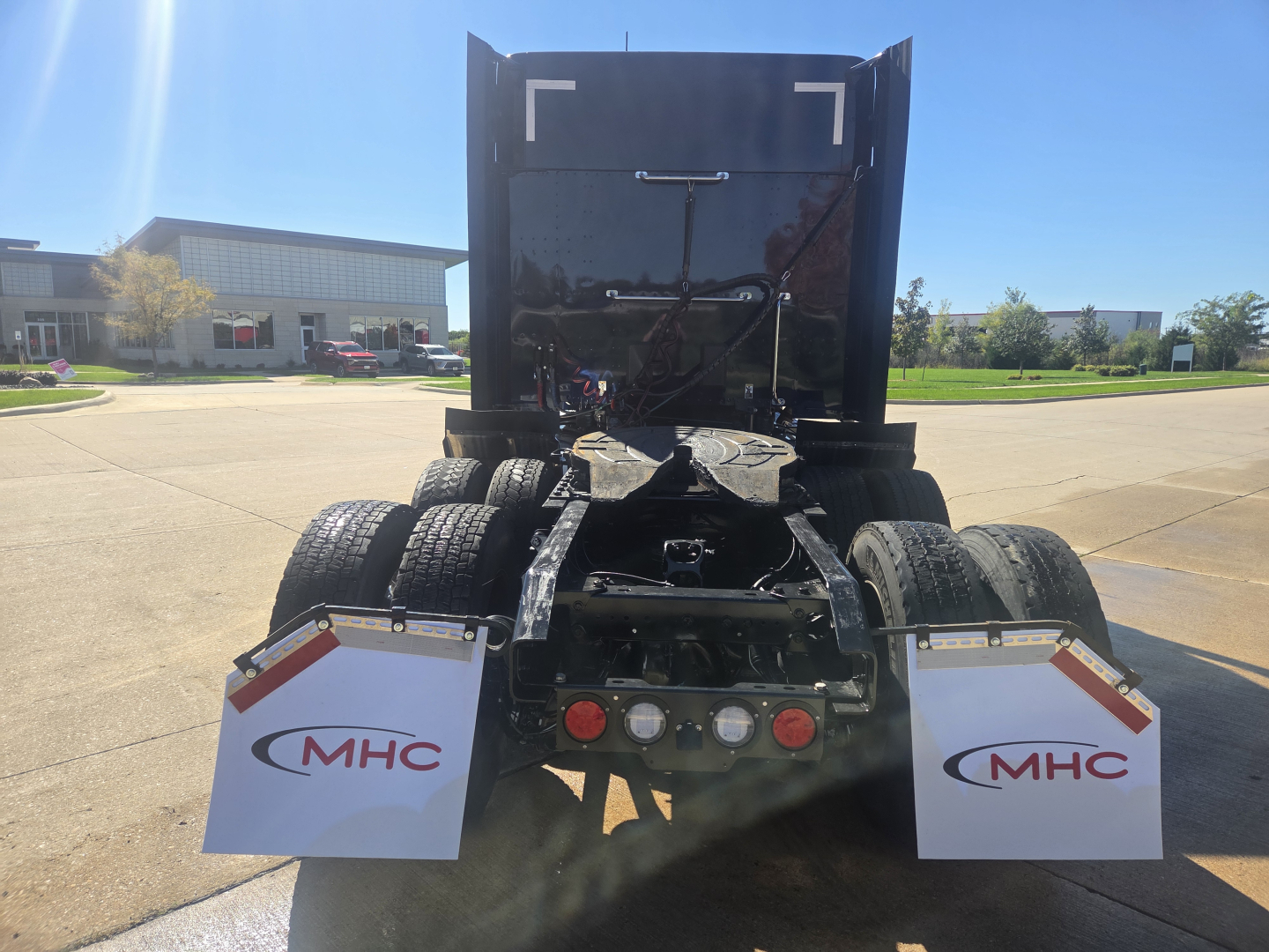 Rear view of a Kenworth W990 truck chassis showing dual rear axles and MHC mud flaps.
