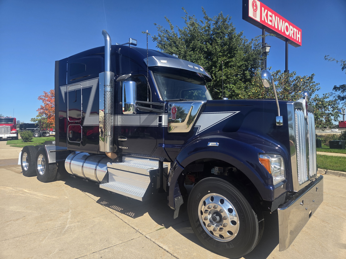 Kenworth W990 heavy-duty truck side view showing chrome exhaust stacks and grille with blue and silver paint.