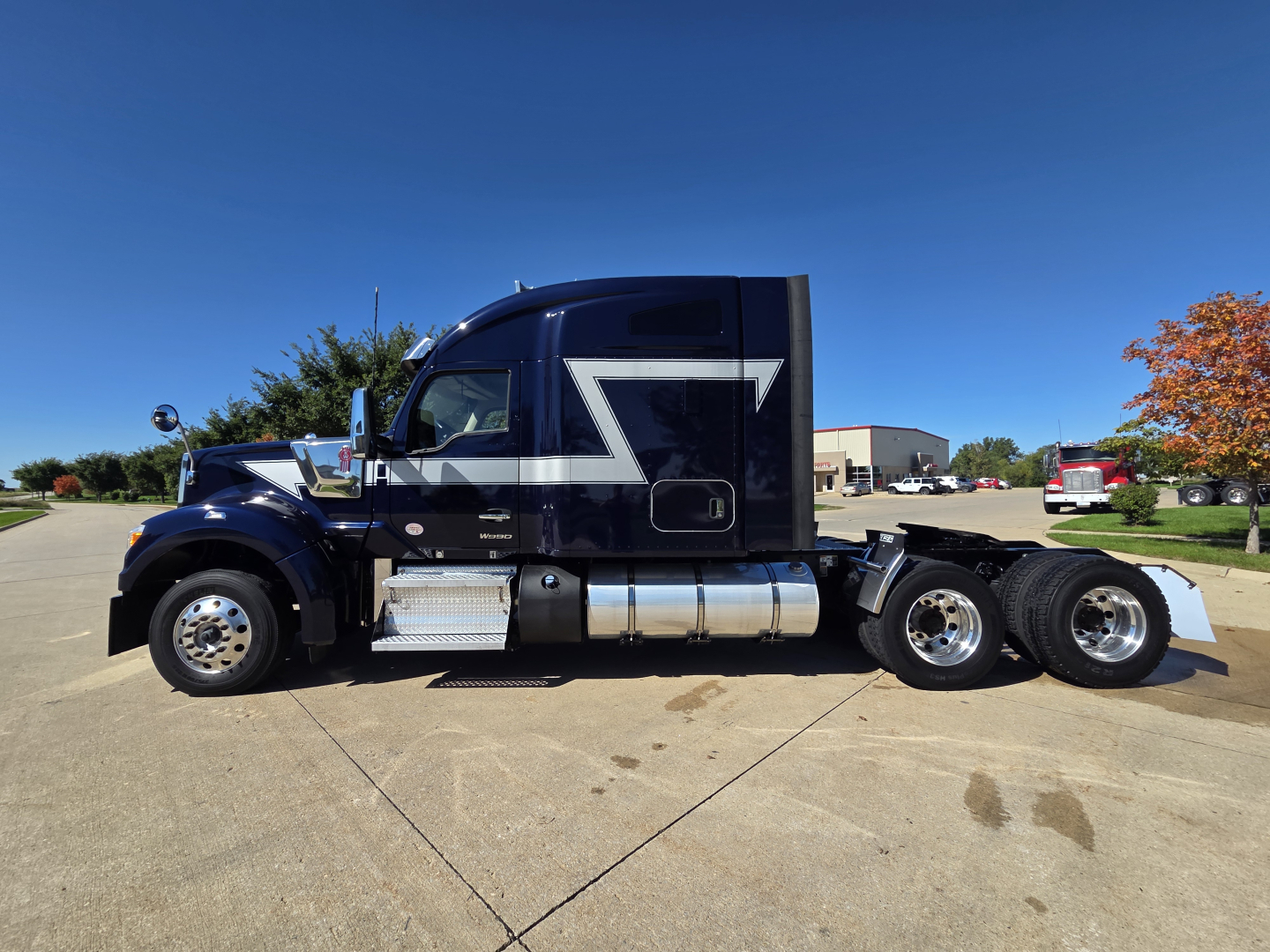 Kenworth W990 conventional sleeper truck side view showing dark blue paint with silver chrome fuel tanks and wheel hubs.