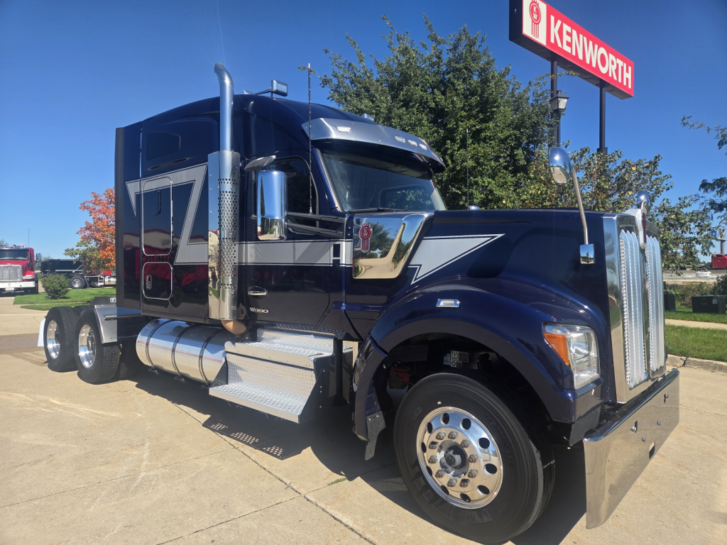 Kenworth W990 heavy-duty truck side view showing chrome exhaust stacks and grille with blue and silver paint.