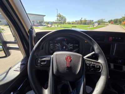 Kenworth W990 cabin steering wheel and dashboard view from driver seat, front windshield with side mirrors, infotainment and controls visible.