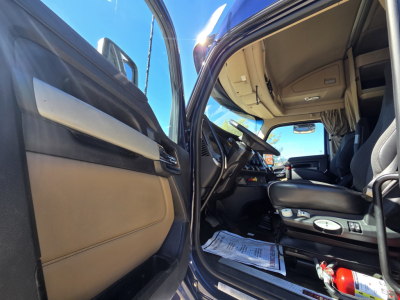 Kenworth W990 cab interior with open door, steering wheel, dashboard, and driver's seat visible; paper on floor mat and fire extinguisher at footwell.