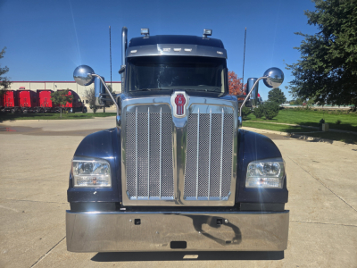 Kenworth W990 front view showing large chrome grille, dual round mirrors, and chrome bumper; front hood and windshield with peak cab; no text visible.