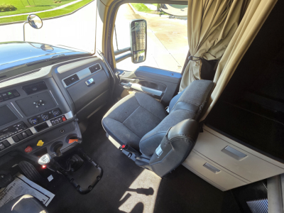 Kennworth W990 truck interior front cabin view with driver seat, steering wheel, dashboard, and side window; curtain visible by sleeper area.