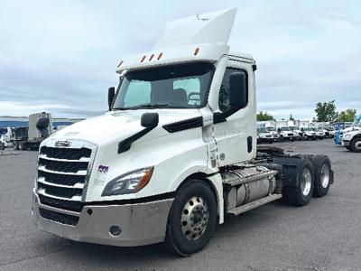 Freightliner Cascadia 126 daycab tractor showing front left side with raised hood and sleeper area, white exterior, dual rear axles, chassis fuel tanks and wheels visible.
