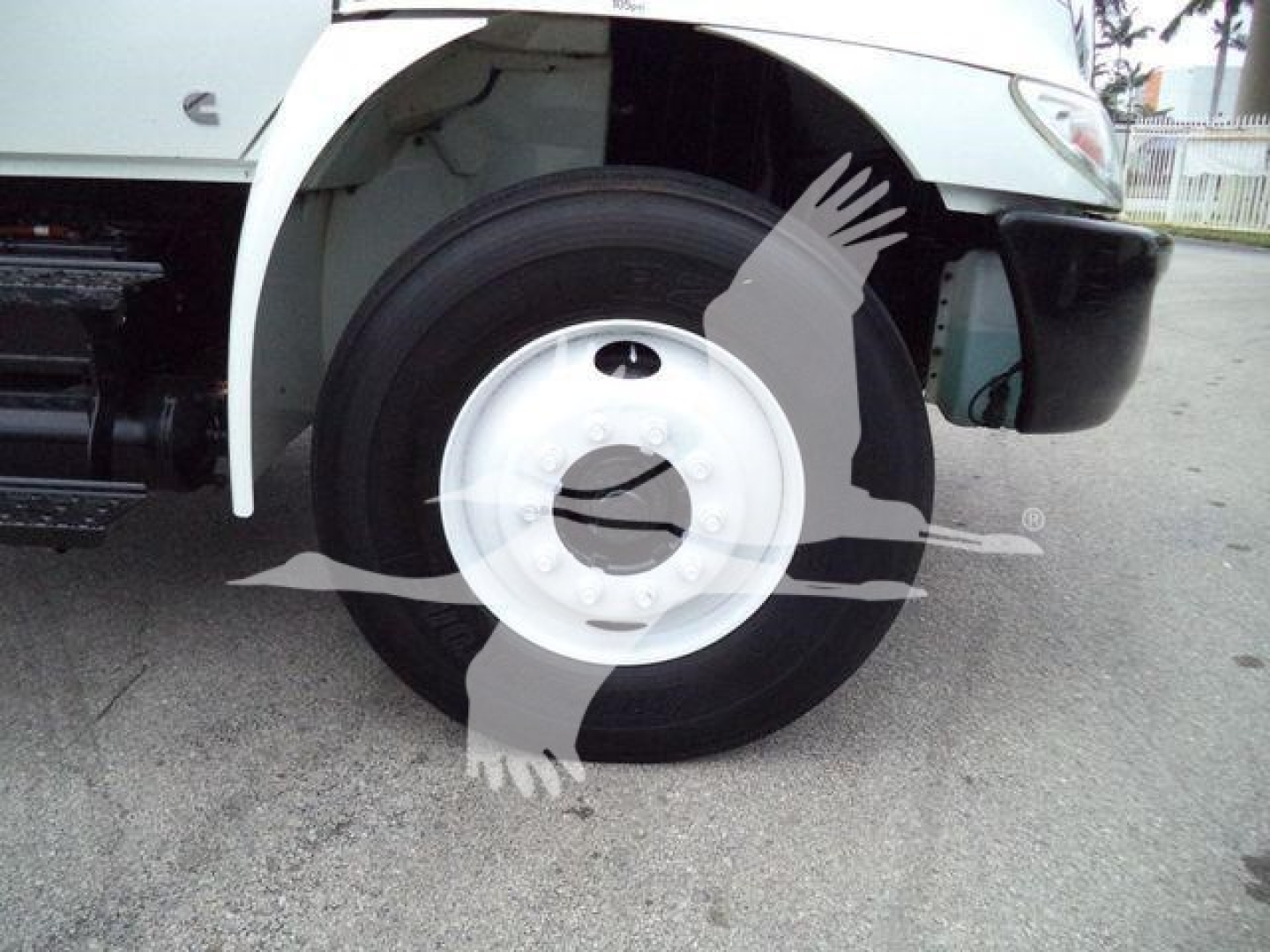 Wheel and front fender area of a 2019 International 4300 box truck showing front wheel, white steel wheel cover, exposed suspension and part of the bumper.