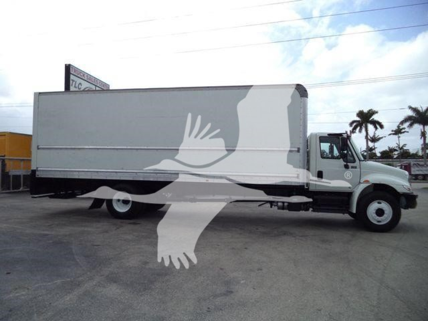 Medium-duty box truck side view showing cargo box with a large logo/watermark and a cab with International emblem; no legible model text visible.