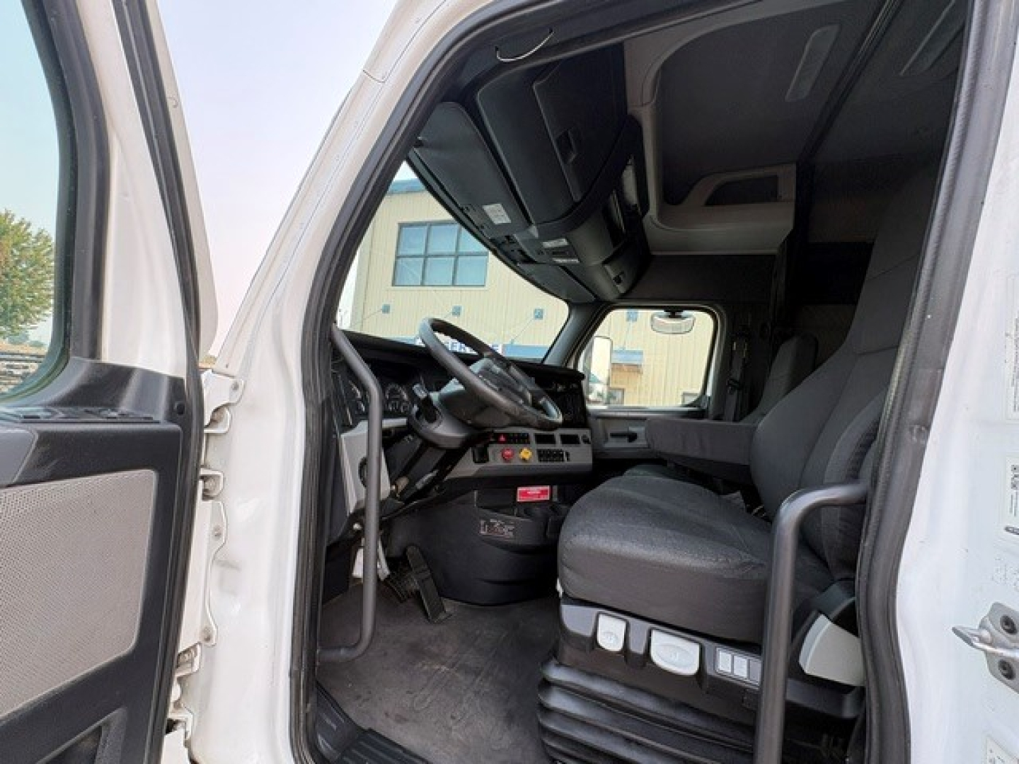 Cab interior of a 2020 Freightliner Cascadia 126 truck showing driver seat with control panels, steering wheel, and dashboard visible through open door.