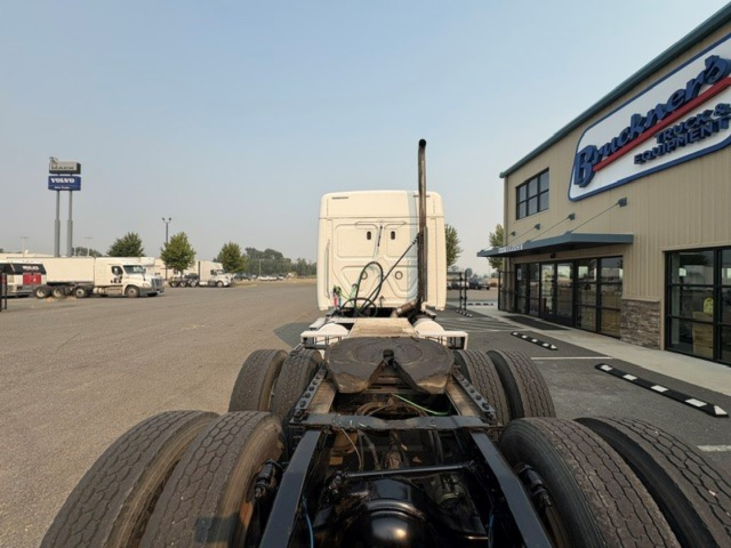 Truck cab behind view showing fifth wheel and rear wheels of a Freightliner Cascadia 126 tractor chassis, sleeper cab in distance at a dealership lot.