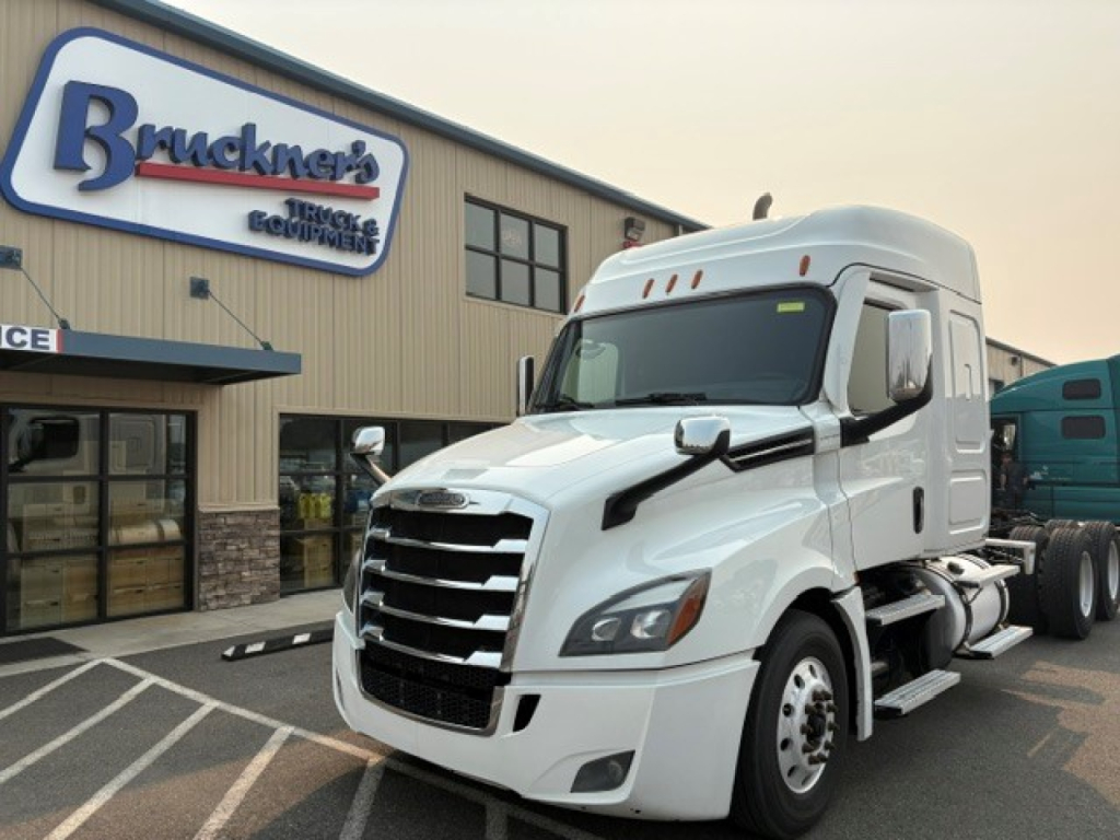 Truck in front of a dealership showing a white Freightliner Cascadia 126 semi-truck cab with grille and side mirrors