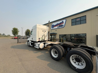 Truck chassis and cab of a Freightliner Cascadia 126 semi-truck in a dealership lot, with the cab and exposed rear dual axles.