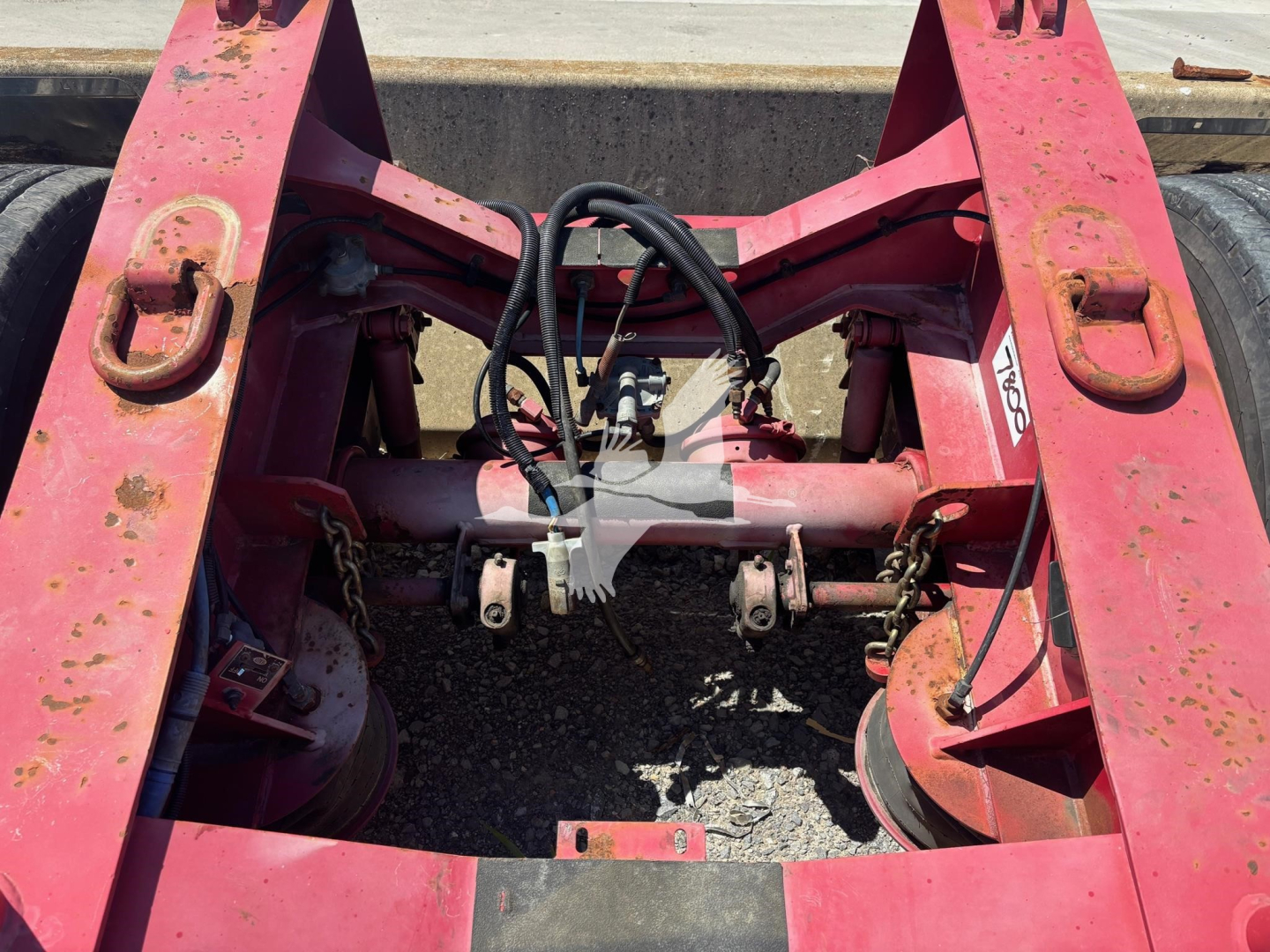 Dolly trailer chassis rear view showing pink frame, hydraulic hoses, and fifth-wheel area with coupler hardware and brackets.