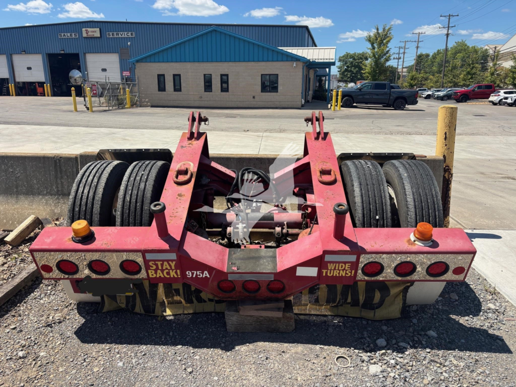 Trailer rear showing Fontaine flip axle with dual axles and tires, caution lights, and labels 'STAY BACK!' and 'WIDE TURNS' on red frame.