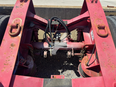 Dolly trailer chassis rear view showing pink frame, hydraulic hoses, and fifth-wheel area with coupler hardware and brackets.
