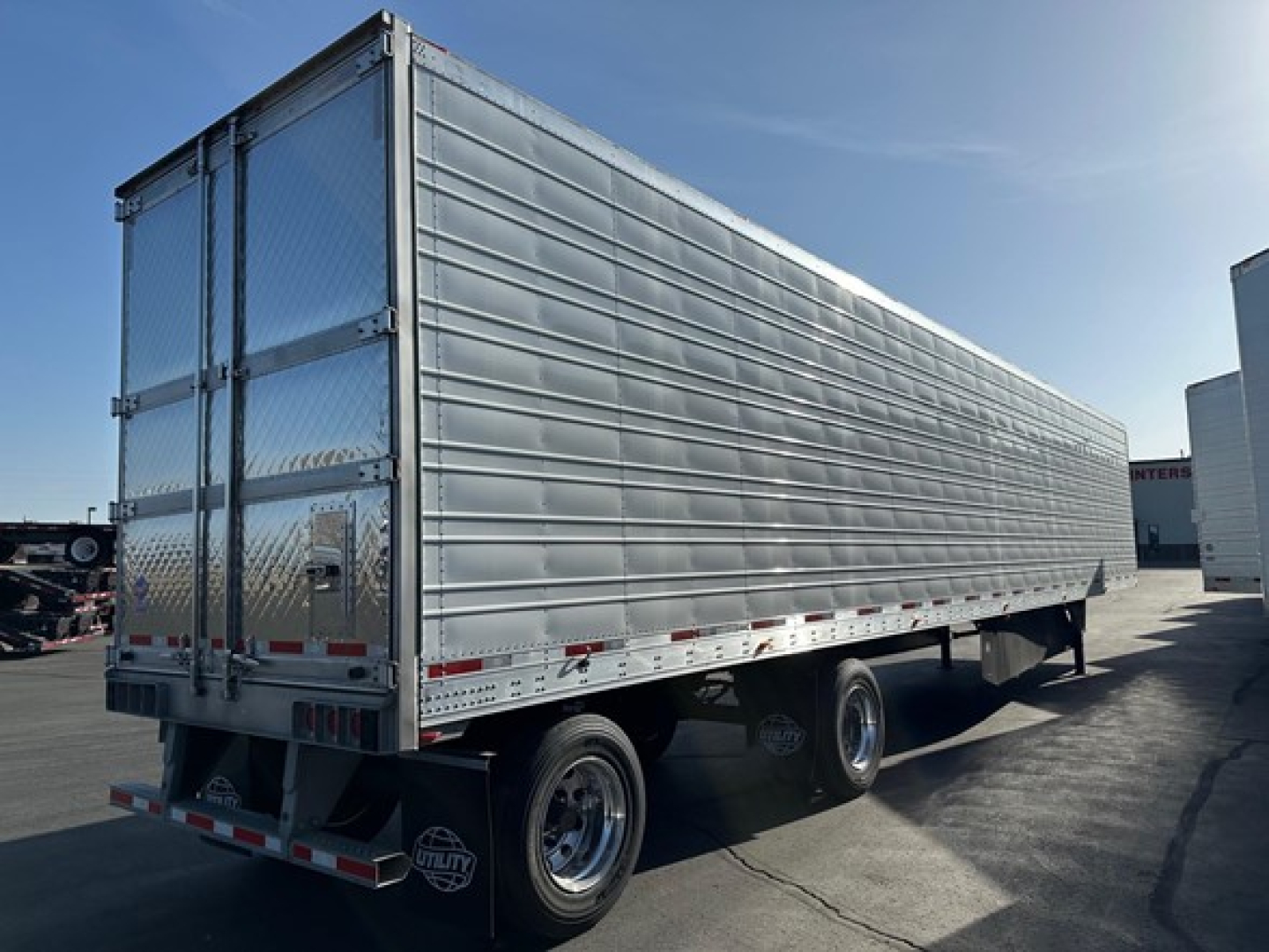 Trailer side view showing aluminum riveted walls and dual rear doors of a 2026 Utility 3000R reefer trailer with diamond plate rear bumper and chrome wheels.