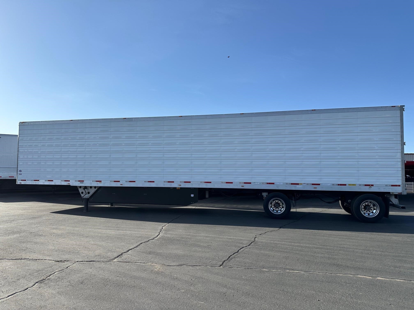 Long white refrigerated trailer with raised side panels and dual rear axles parked on pavement.