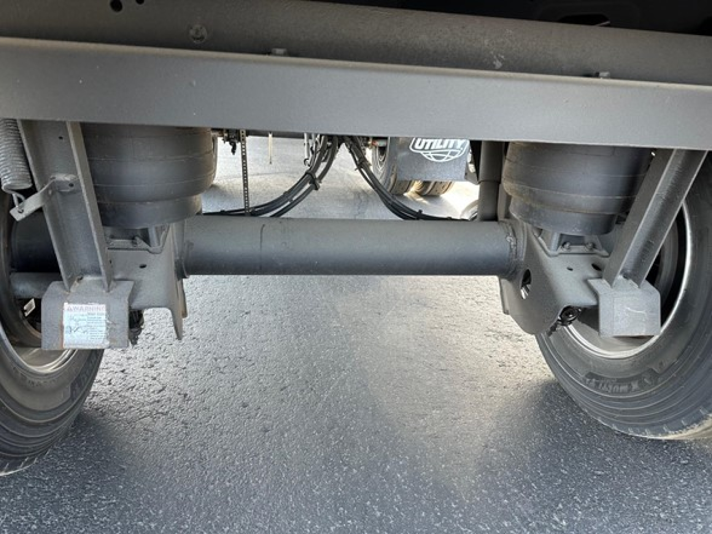 Rear view of a 2026 Utility 3000R trailer hitch area showing tandem axles, suspension, air lines, and frame crossmember.