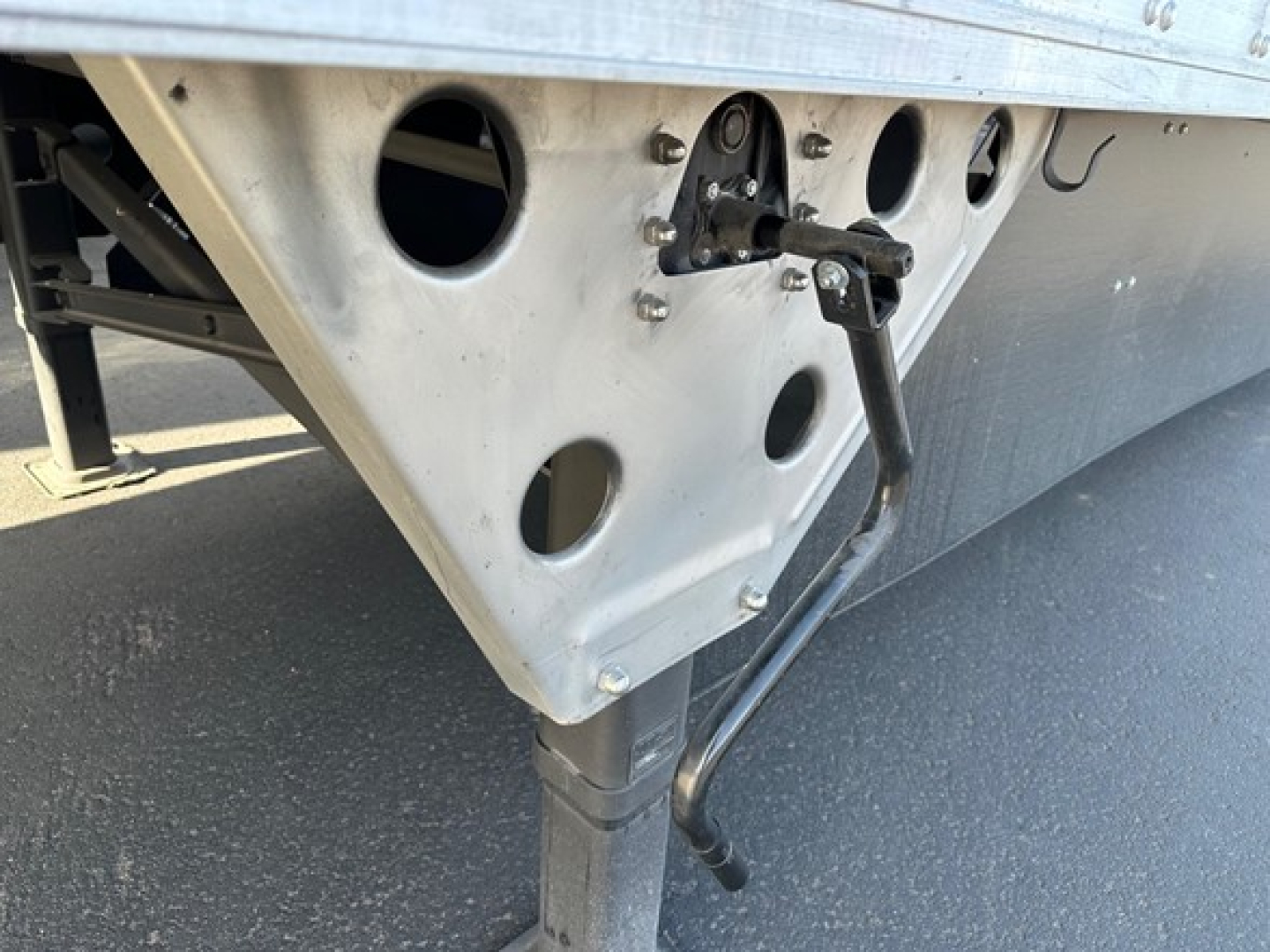 Trailer corner showing support leg and lifting hook with metal perforated bracket on a utility trailer side panel.