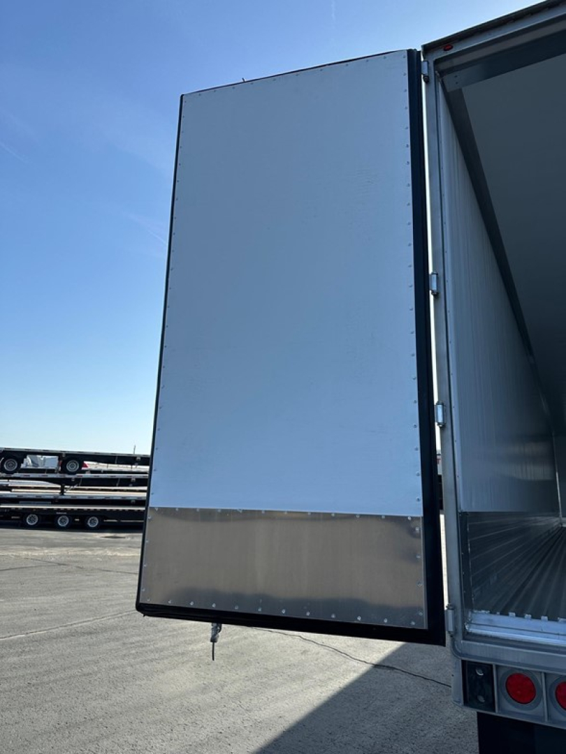 Utility 3000R trailer rear door open showing interior metal walls and outside hinge; blue sky.