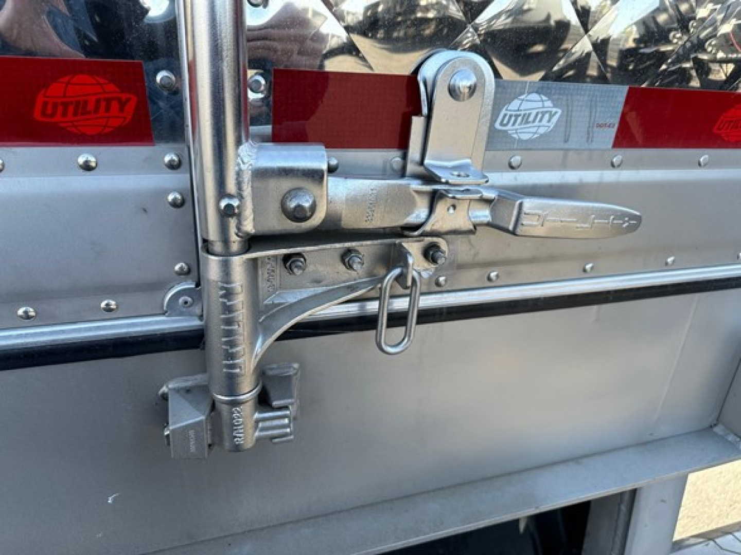 Trailer rear door latch and hasp on a 2026 Utility 3000R reefer trailer showing metal latches, hinges, and reflective red/white stickers with Utility logo.