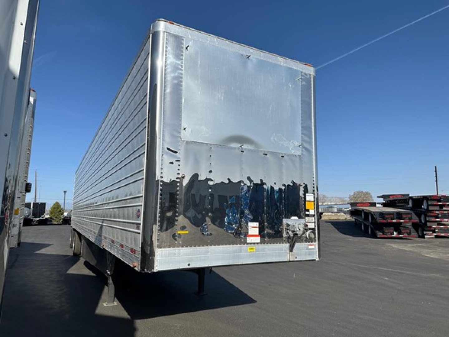 Utility 3000R trailer rear view showing stainless rear doors, reflective surfaces, and support legs in a dealership lot.