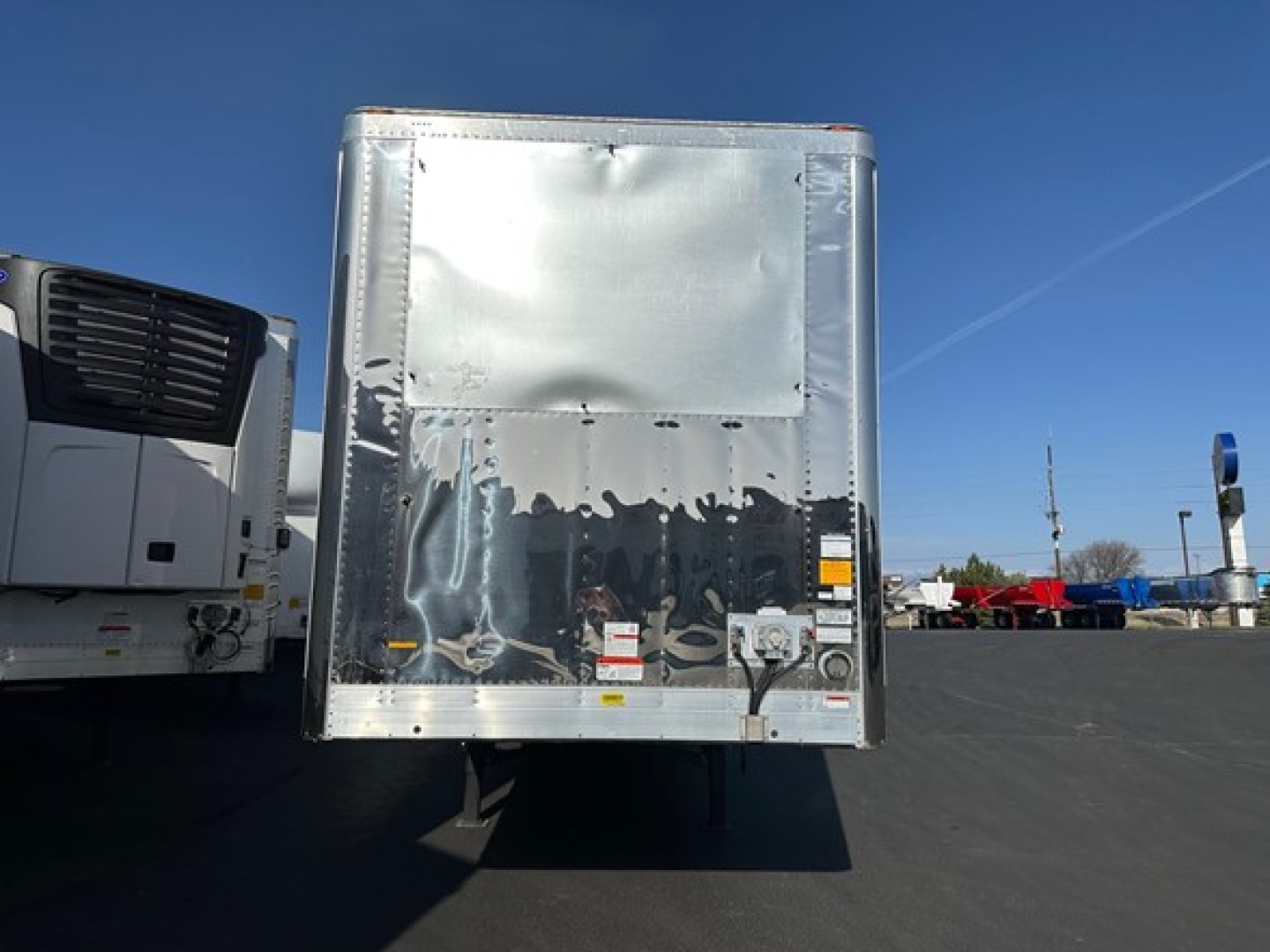 Utility 3000R trailer rear view showing reflective aluminum surface and rear door, with surrounding lot and other trailers.